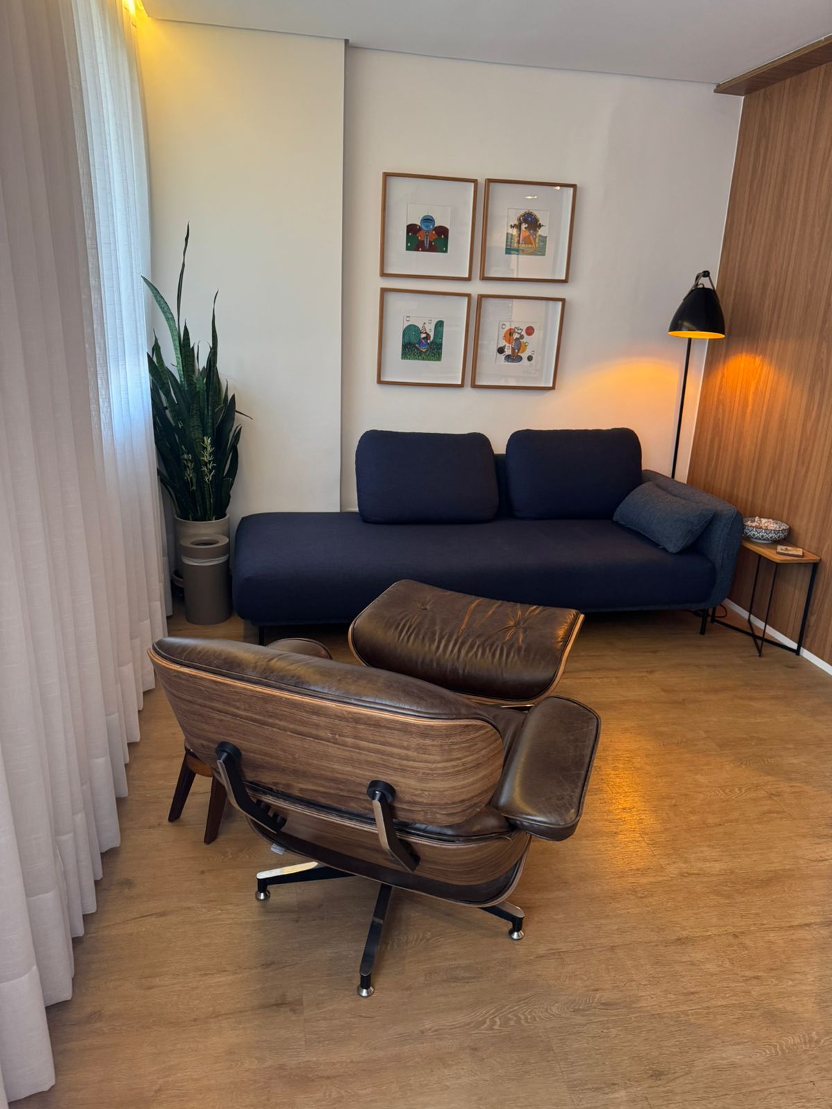 Poltrona Eames vista de trás com sofá azul e quadros na parede